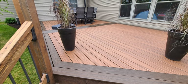 Spacious wooden deck with potted plants, attached to house with white siding and windows visible in background
