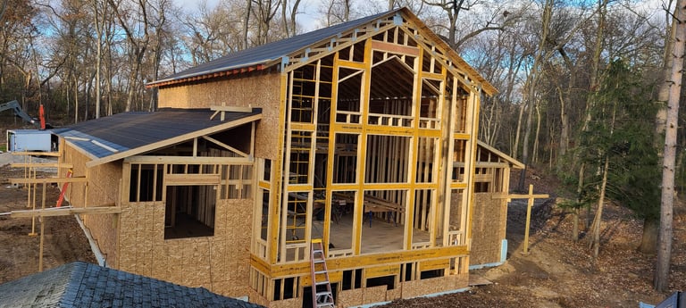 Residential house under construction with exposed wooden framing and brick facade in a wooded area
